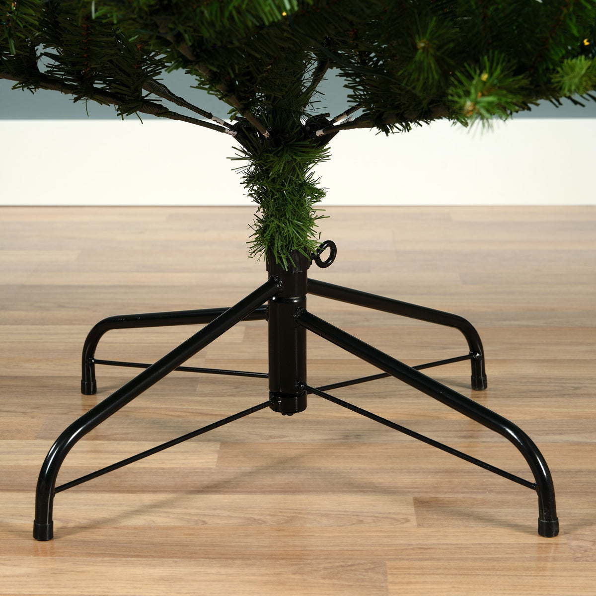 Black metal tree stand with a Christmas tree on a wooden floor.