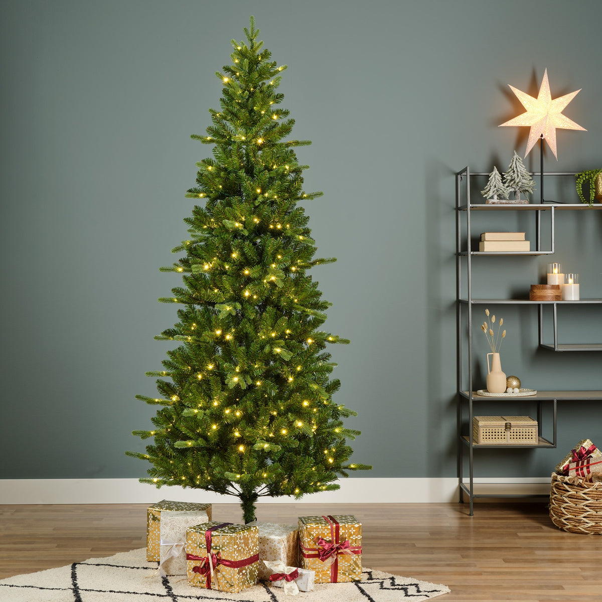 Pre-lit Christmas tree in a room with shelving and wrapped presents beneath